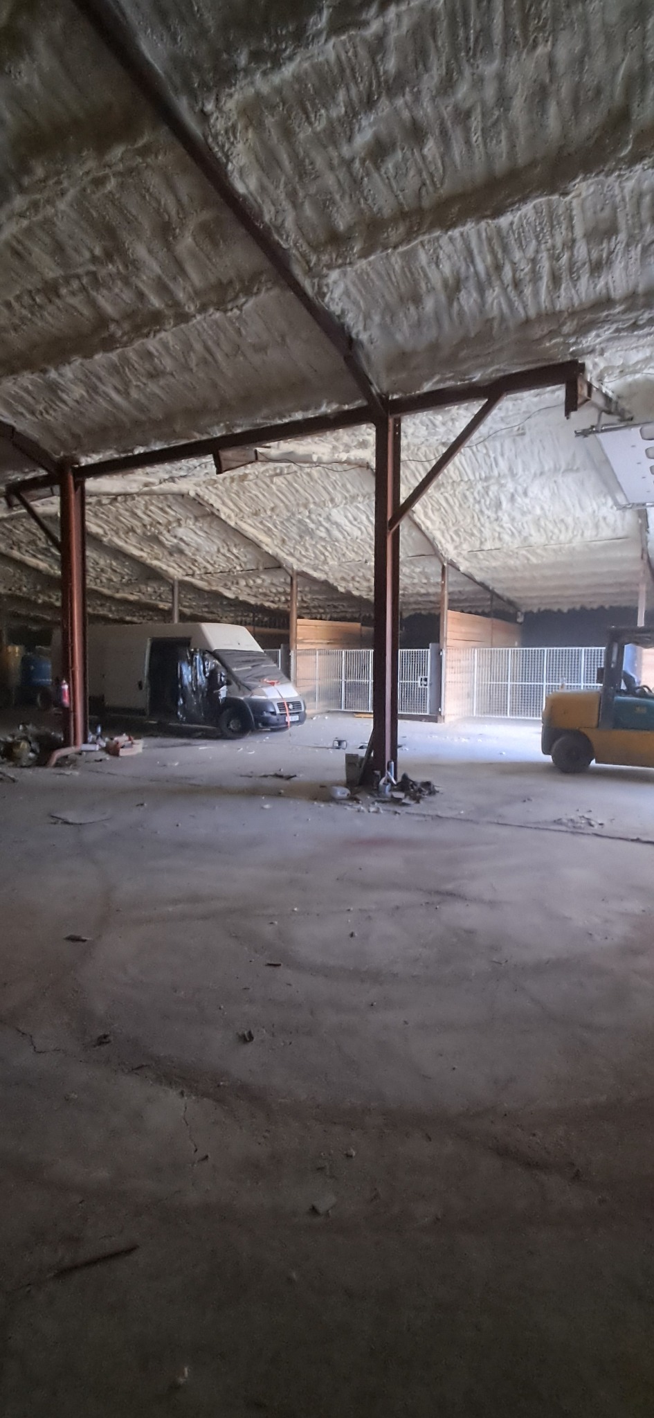 Wnętrze hali z ocieplonym pianką PUR dachem, widoczne stalowe konstrukcje, samochód dostawczy i wózek widłowy w tle. Ocieplenie wykonane natryskowo.