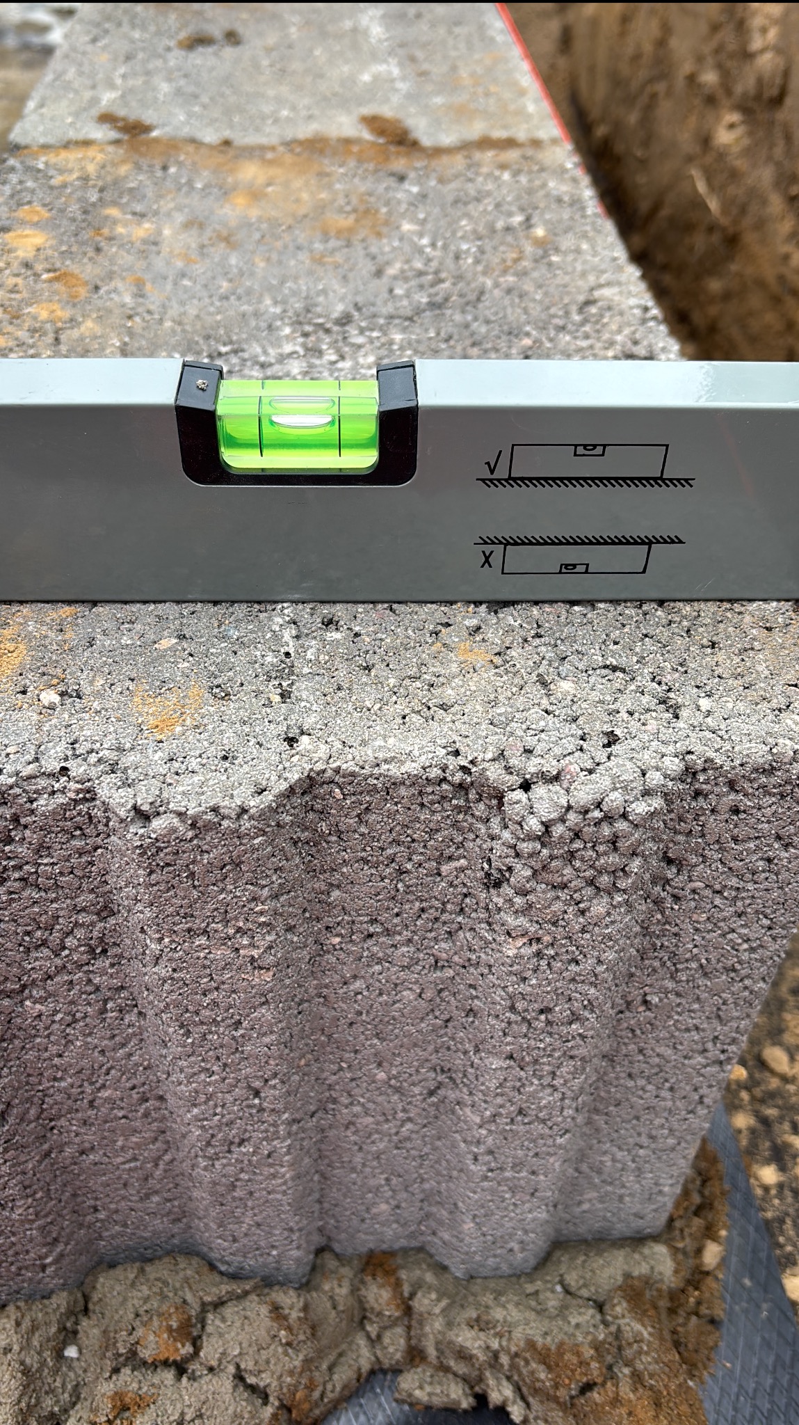 Poziomica na bloku z betonu komórkowego o falistej strukturze, ustawionym na fundamencie. Detal z budowy, precyzja pomiaru, zbliżenie na narzędzie i materiał.