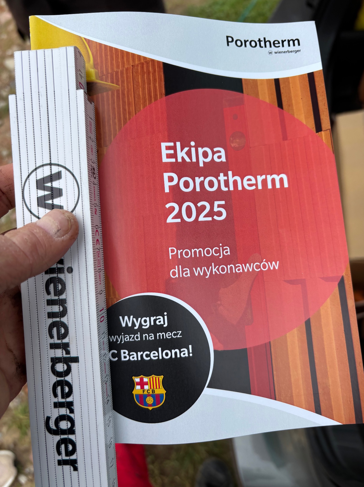 Miernik Wienerberger obok ulotki Porotherm 'Ekipa Porotherm 2025', promocja dla wykonawców, wygraj wyjazd na mecz FC Barcelona.