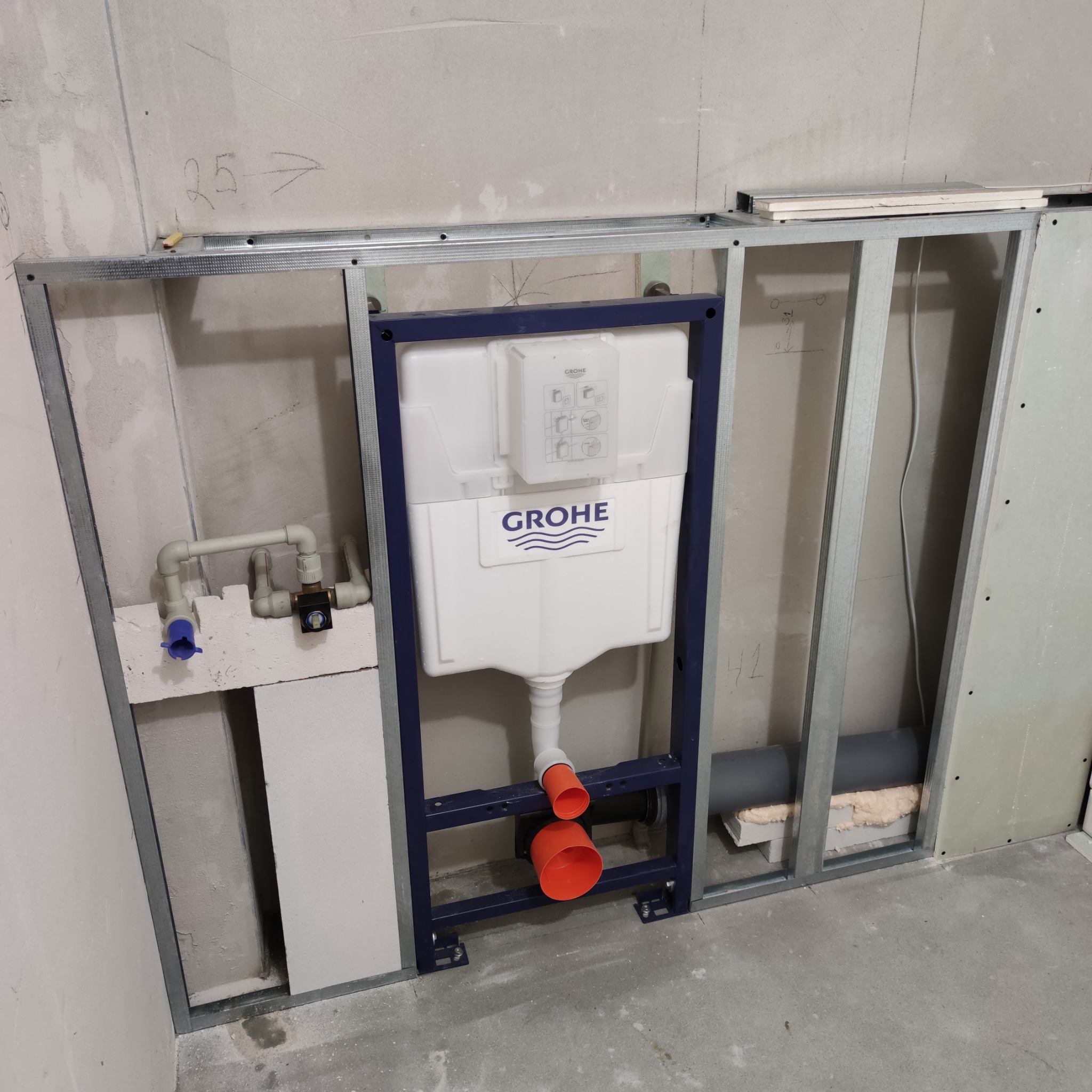 Stelaż podtynkowy Grohe w metalowej konstrukcji, widoczne rury doprowadzające wodę i odpływ. Ściana w surowym stanie, przygotowana do dalszych prac wykończeniowych.