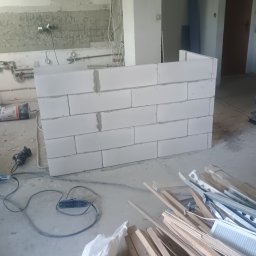 Frontmen - Wnętrze w trakcie remontu: murowana ścianka działowa z białych bloczków, widoczne narzędzia i materiały budowlane, ślady po instalacjach na ścianie.