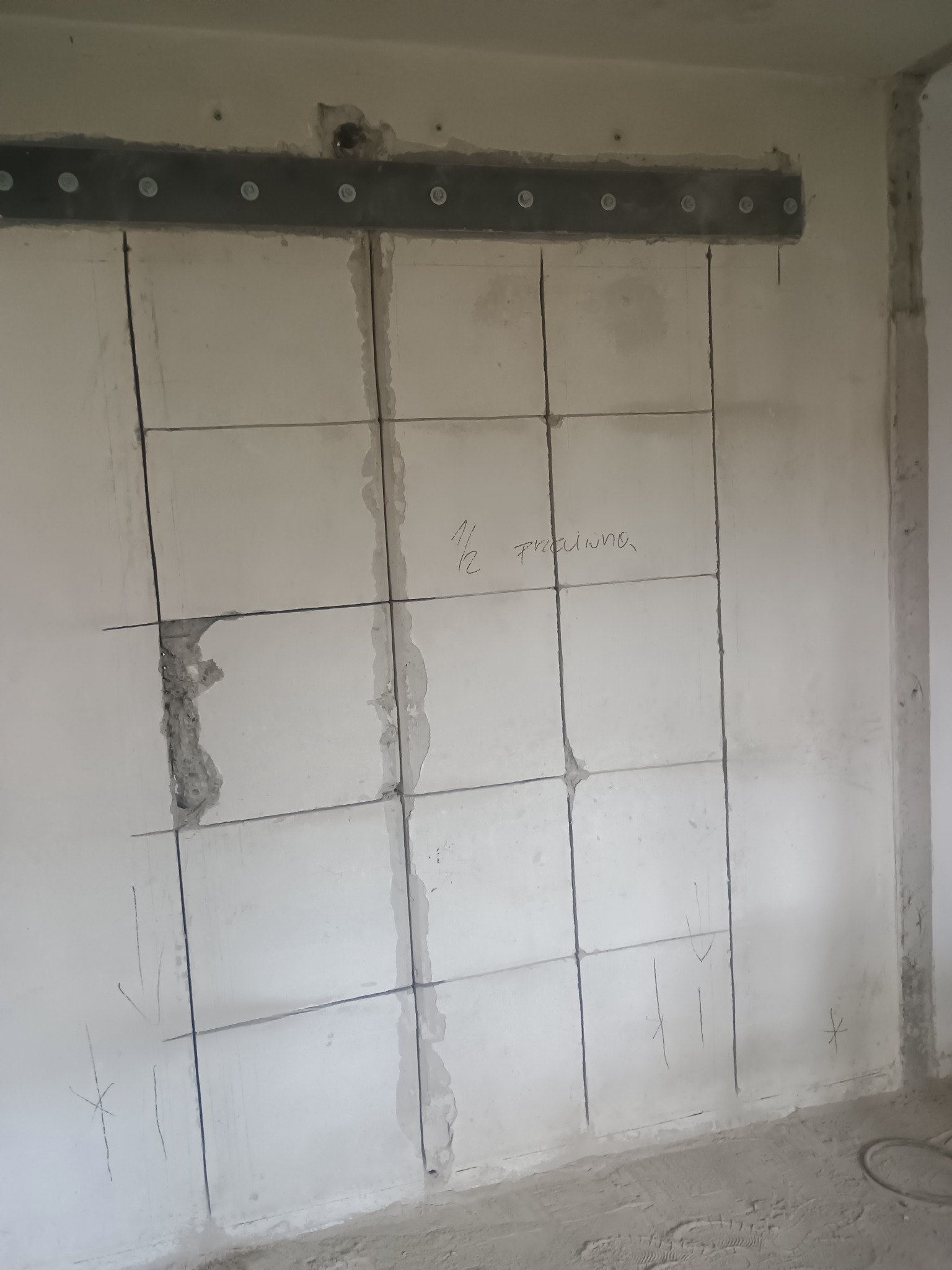 Ściana z betonu komórkowego z wyrysowaną siatką podziału i wzmocnieniem nad nią. Przygotowanie do montażu płytek lub paneli ściennych.