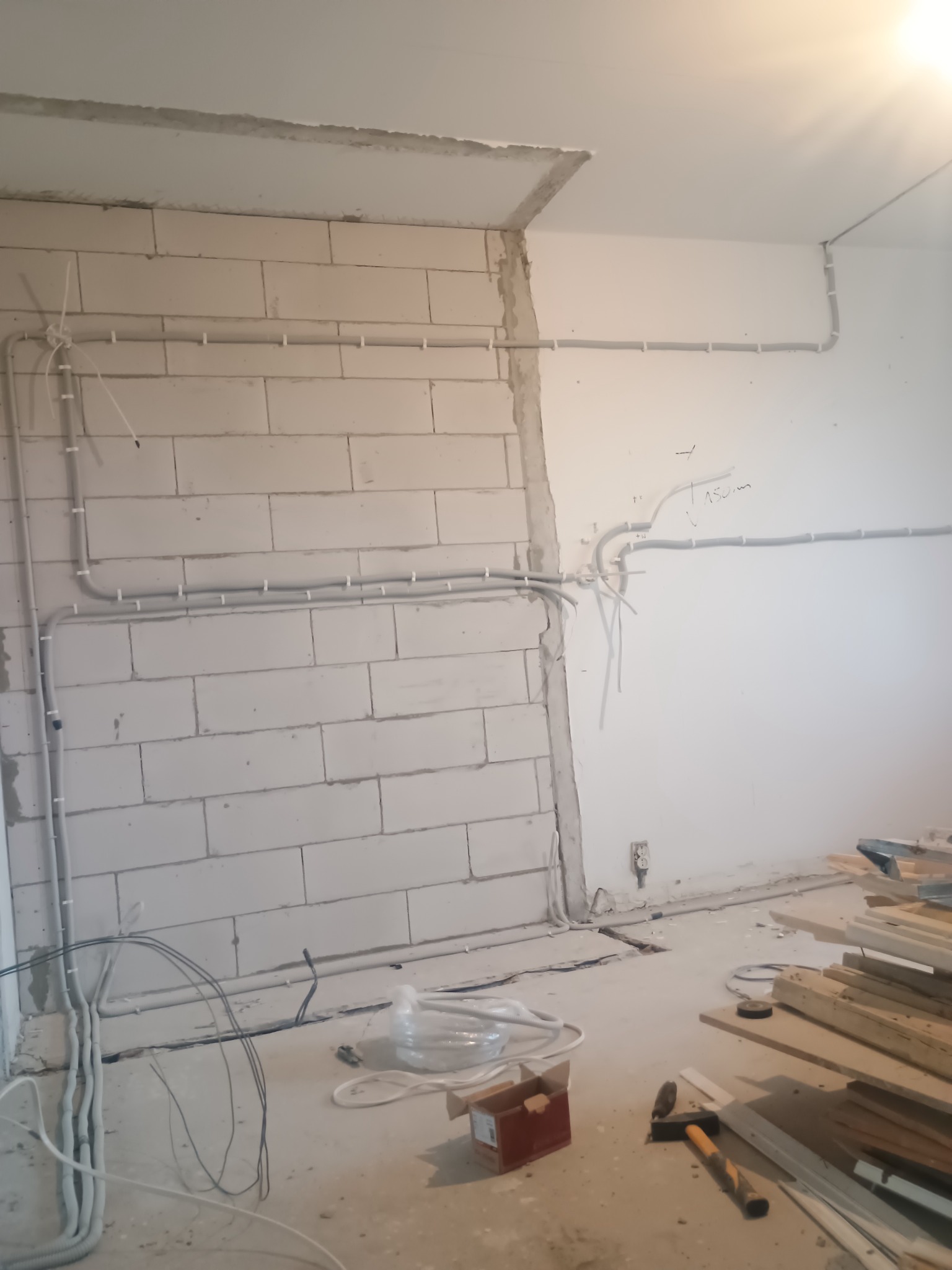 Instalacja elektryczna natynkowa w Zamościu, widoczna na ścianie z bloczków i na ścianie z białym tynkiem. Na podłodze narzędzia i materiały budowlane.