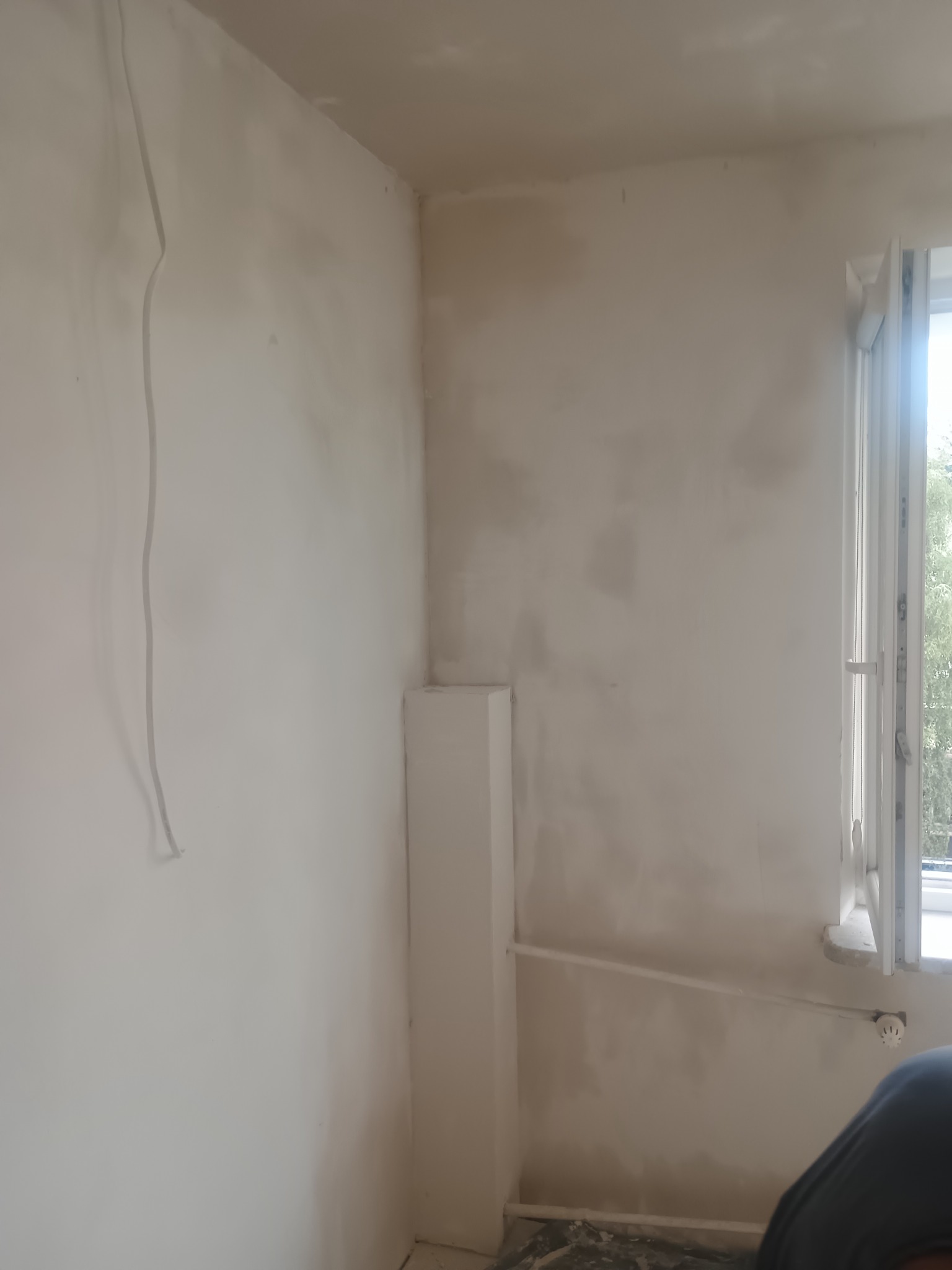 Pokój w trakcie gruntowania ścian na biało, widoczne kable i fragment okna. Przygotowanie do malowania ścian w pomieszczeniu.