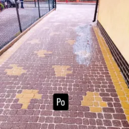 Świeżo ułożona kostka brukowa w odcieniach brązu i żółci, tworząca wzór na ścieżce. Część kostki jest jeszcze mokra, co sugeruje niedawne mycie lub opady.