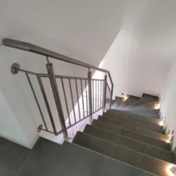 Nowoczesna, metalowa balustrada schodowa z podświetlanymi stopniami. Szare płytki na schodach i minimalistyczny design.