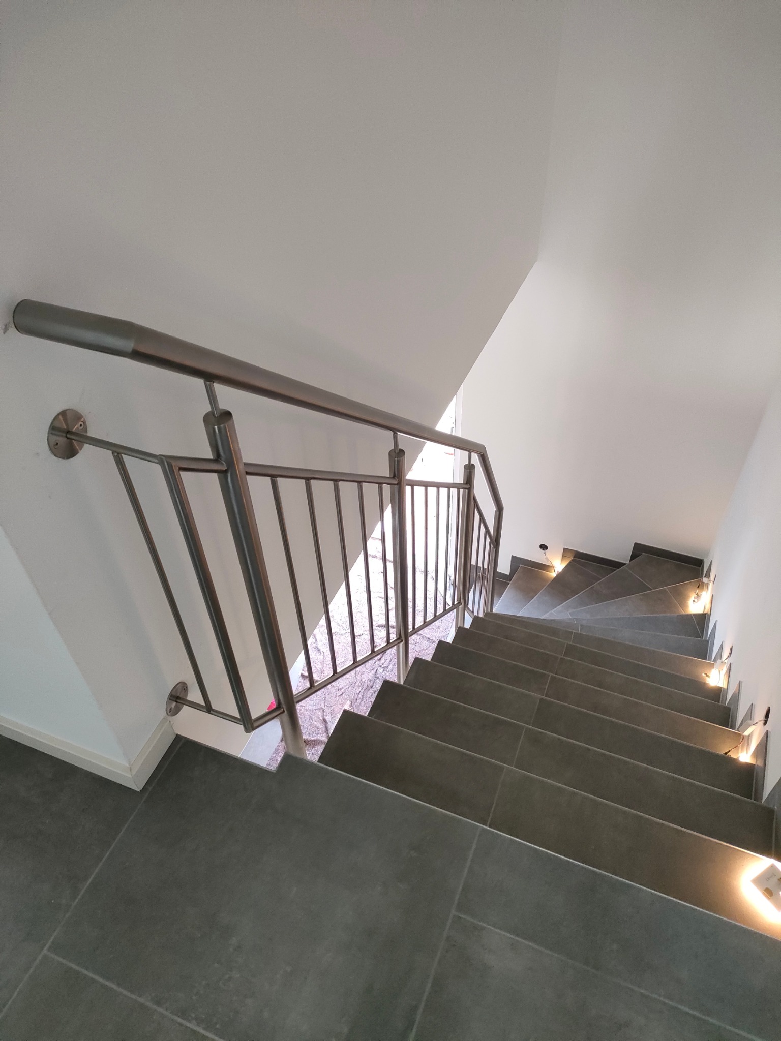 Nowoczesna, metalowa balustrada schodowa z podświetlanymi stopniami. Szare płytki na schodach i minimalistyczny design.