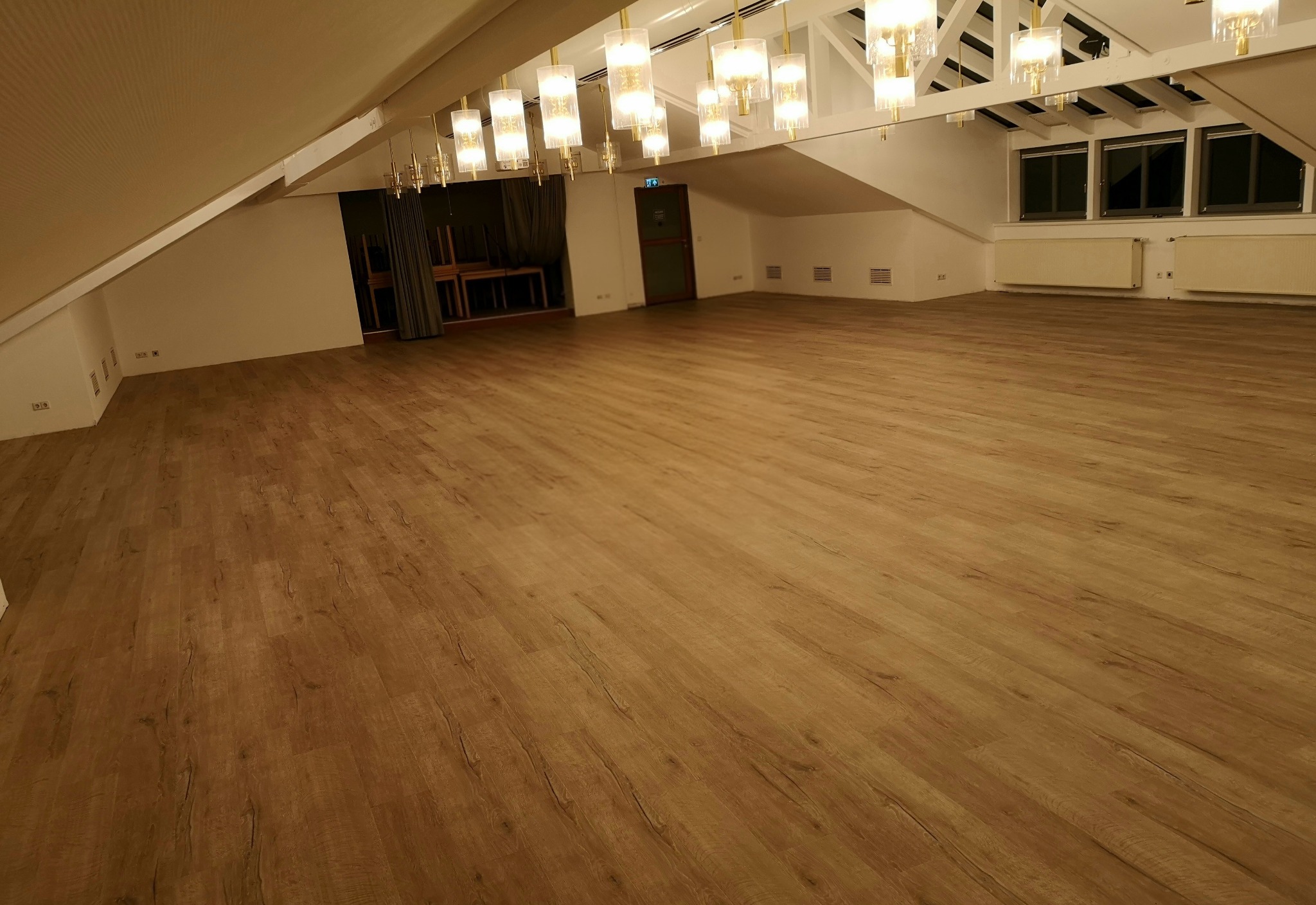 Jasna, drewnopodobna podłoga winylowa LVT w przestronnym, oświetlonym wnętrzu poddasza z białymi ścianami i dekoracyjnymi lampami.