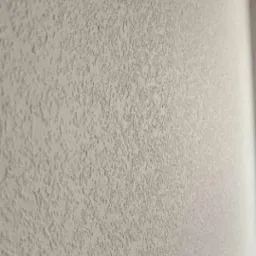 Ściana pokryta jasną, strukturalną gładzią o wyraźnej fakturze, widoczna pod kątem. Wykończenie ściany w odcieniach beżu i szarości, z delikatnym cieniowaniem.