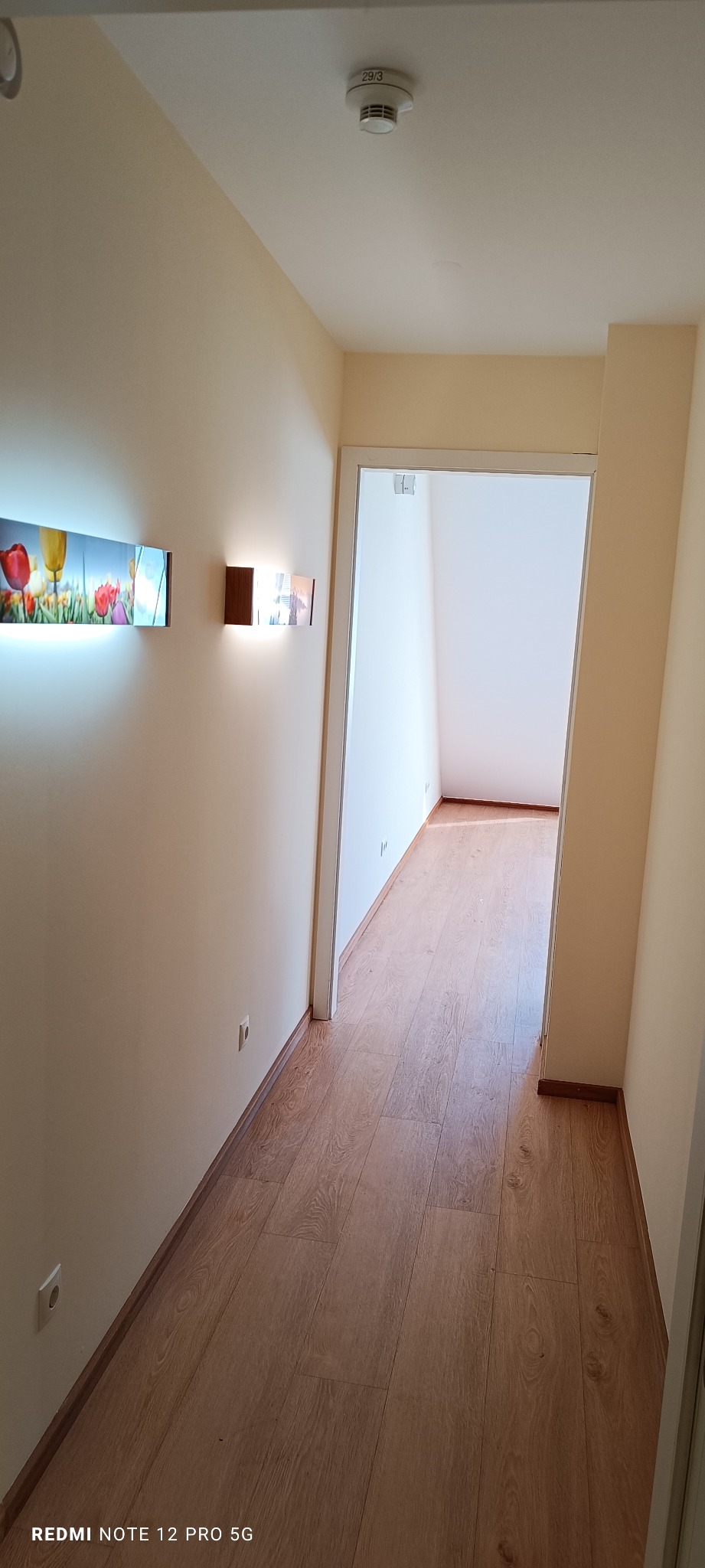 Korytarz po remoncie z panelami podłogowymi w odcieniach brązu. Na ścianie nowoczesne oświetlenie i obraz z motywem tulipanów. Widok z perspektywy wejścia do pomieszczenia.