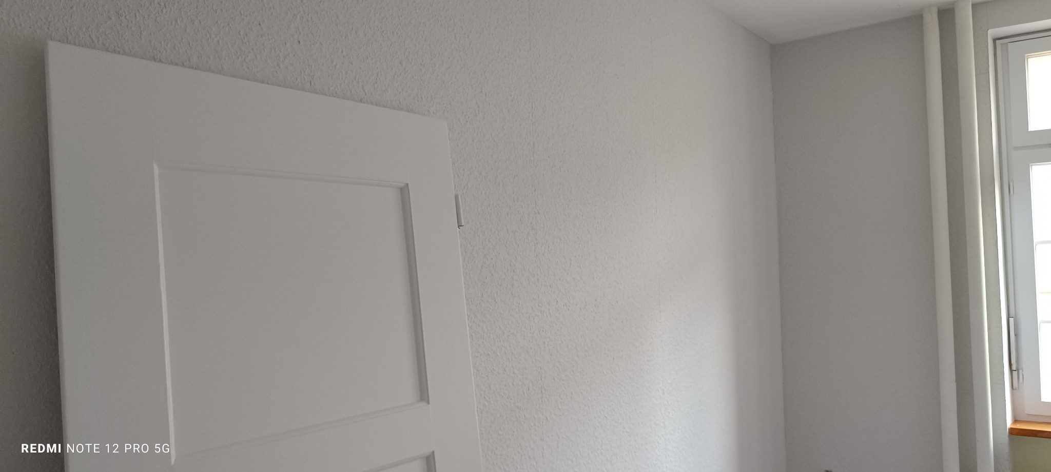 Białe, odświeżone wnętrze po remoncie: gładkie ściany pomalowane na biało, widoczna biała stolarka drzwiowa i okienna. Minimalistyczny design po renowacji.