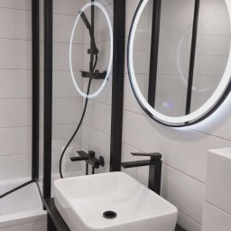Milimetr Kwadrat - Remonty i wykończenia Piotr Stróżewski - Nowoczesna łazienka z białą umywalką nablatową, czarną armaturą i okrągłym lustrem z podświetleniem LED. Minimalistyczny design z płytkami imitującymi drewno.