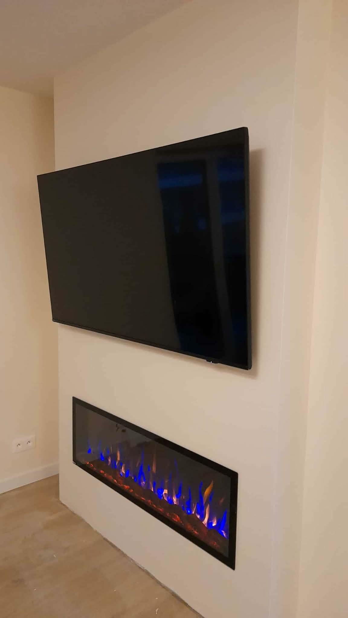 Nowoczesny salon z zamontowanym telewizorem i podłużnym kominkiem elektrycznym z niebiesko-pomarańczowymi płomieniami, w minimalistycznym wnętrzu.