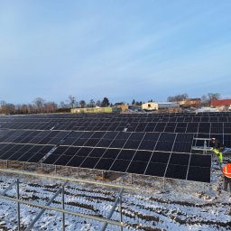 MARBOG - Rozległa farma paneli słonecznych w zimowym krajobrazie, z pracownikami w odblaskowych ubraniach podczas instalacji. Częściowo zasypana śniegiem ziemia.