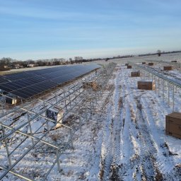 MARBOG - Montaż farmy fotowoltaicznej na zaśnieżonym terenie. Widoczne rzędy paneli i stalowa konstrukcja. Ślady opon na śniegu. Błękitne niebo w tle.