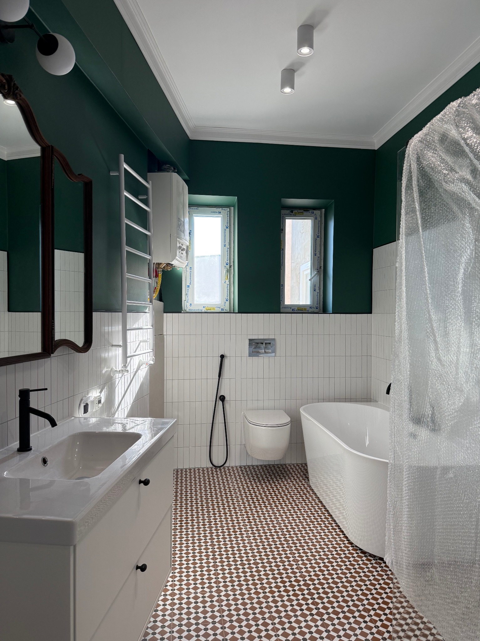 Nowoczesna łazienka w odcieniach bieli i butelkowej zieleni. Uwagę przykuwają wzorzyste płytki podłogowe i designerska armatura. Widoczne okna z białymi ramami.