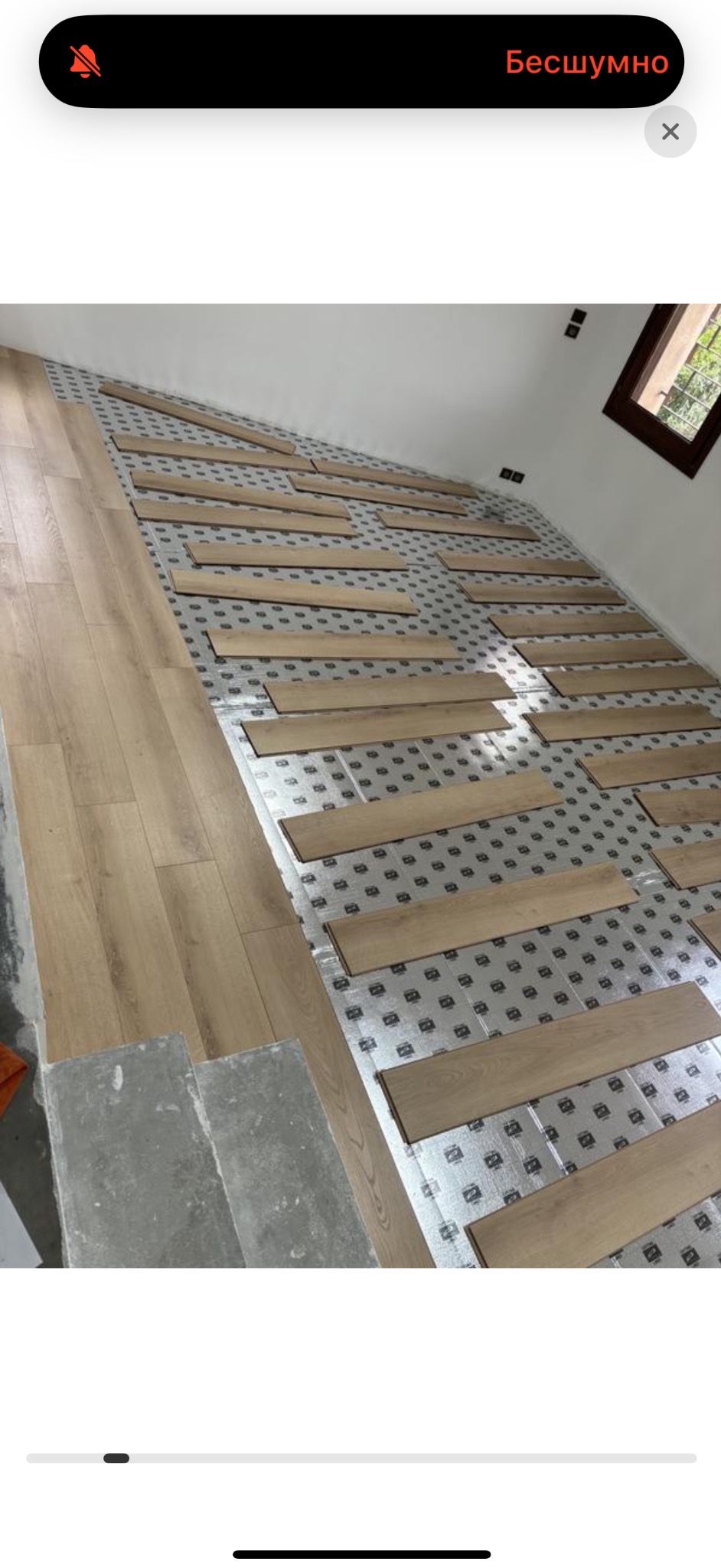 Układanie paneli podłogowych na podkładzie w jasnym wnętrzu. Widoczny fragment okna i surowe wykończenie ścian.