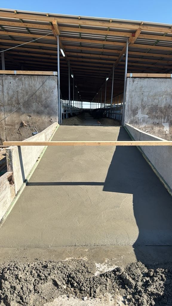 Wylewka betonowa wewnątrz konstrukcji hali z drewnianym dachem, widok z perspektywy, z deską poziomującą i stertą ziemi w kadrze.