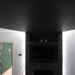 Jakub Porządnicki Porządny Remont - Ciemna ściana z cegły z wnęką na telewizor i oświetleniem LED, na tle jasnych ścian i podłogi. Widoczny fragment sufitu i drzwi do innego pomieszczenia.