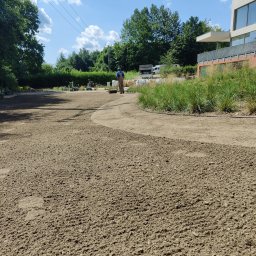 JDG Andriy Grytsenko - Przygotowany teren pod trawnik z wytyczonymi ścieżkami. Pracownik wyrównuje podłoże walcem na tle zieleni i nowoczesnej architektury w słoneczny dzień.