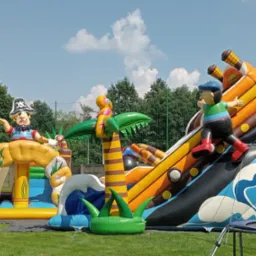 Kolorowy, rozbudowany dmuchany plac zabaw w pirackim stylu z postaciami piratów i palmami na trawiastym terenie, idealny na imprezy plenerowe dla dzieci.