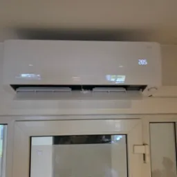 Biała klimatyzacja typu split, model Mirai, zamontowana nad oknem. Widoczny wyświetlacz z temperaturą 28.5 stopni. Minimalistyczny design i jasne otoczenie.