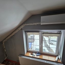 Montaż Klimatyzacji Mont-Instal Łukasz Szczepanek - Klimatyzator Rotenso zamontowany w pokoju na poddaszu, widoczne rury zabezpieczone pianką montażową, okno z widokiem na zewnątrz, narzędzia na parapecie.