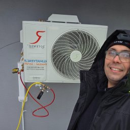 Montaż Klimatyzacji Mont-Instal Łukasz Szczepanek - Instalator uśmiecha się obok zamontowanej klimatyzacji Rotenso HIRO z podłączonymi przewodami serwisowymi i manometrem. Widoczny adres strony internetowej.