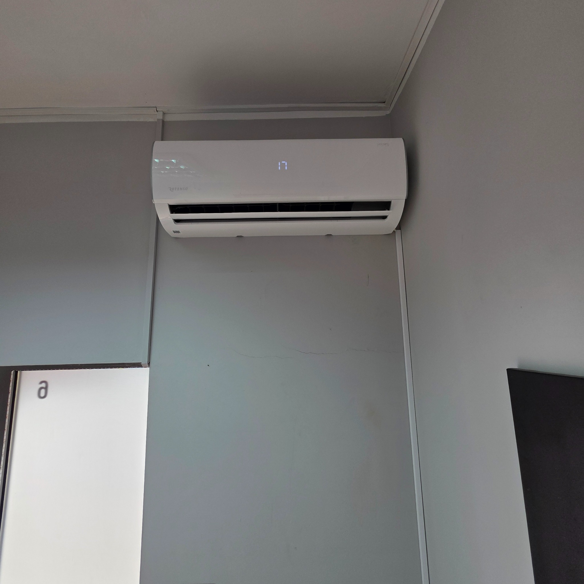 Biały klimatyzator Rotenso zamontowany na szarej ścianie w pomieszczeniu. Na wyświetlaczu widoczna temperatura 17 stopni Celsjusza.