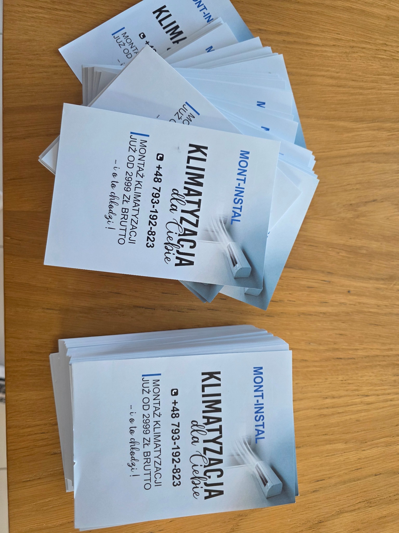 Stos ulotek reklamowych „Mont-Instal” z ofertą montażu klimatyzacji od 2999 zł brutto, leżących na drewnianym blacie. Widoczny numer telefonu i hasło „…i o to chłodzi!”.