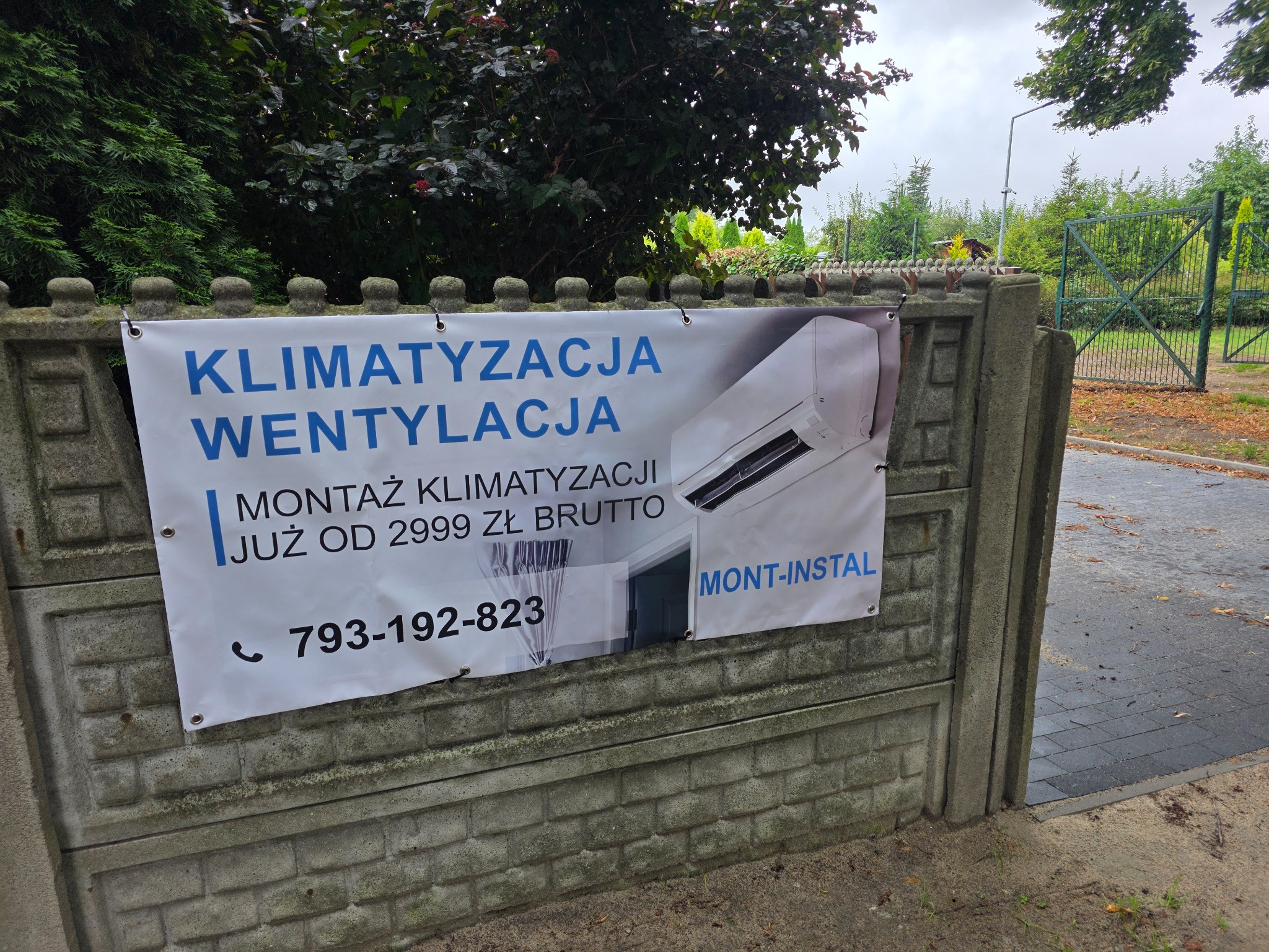 Baner reklamowy na betonowym ogrodzeniu oferujący montaż klimatyzacji i wentylacji od 2999 zł brutto, z numerem telefonu i logiem firmy Mont-Instal.