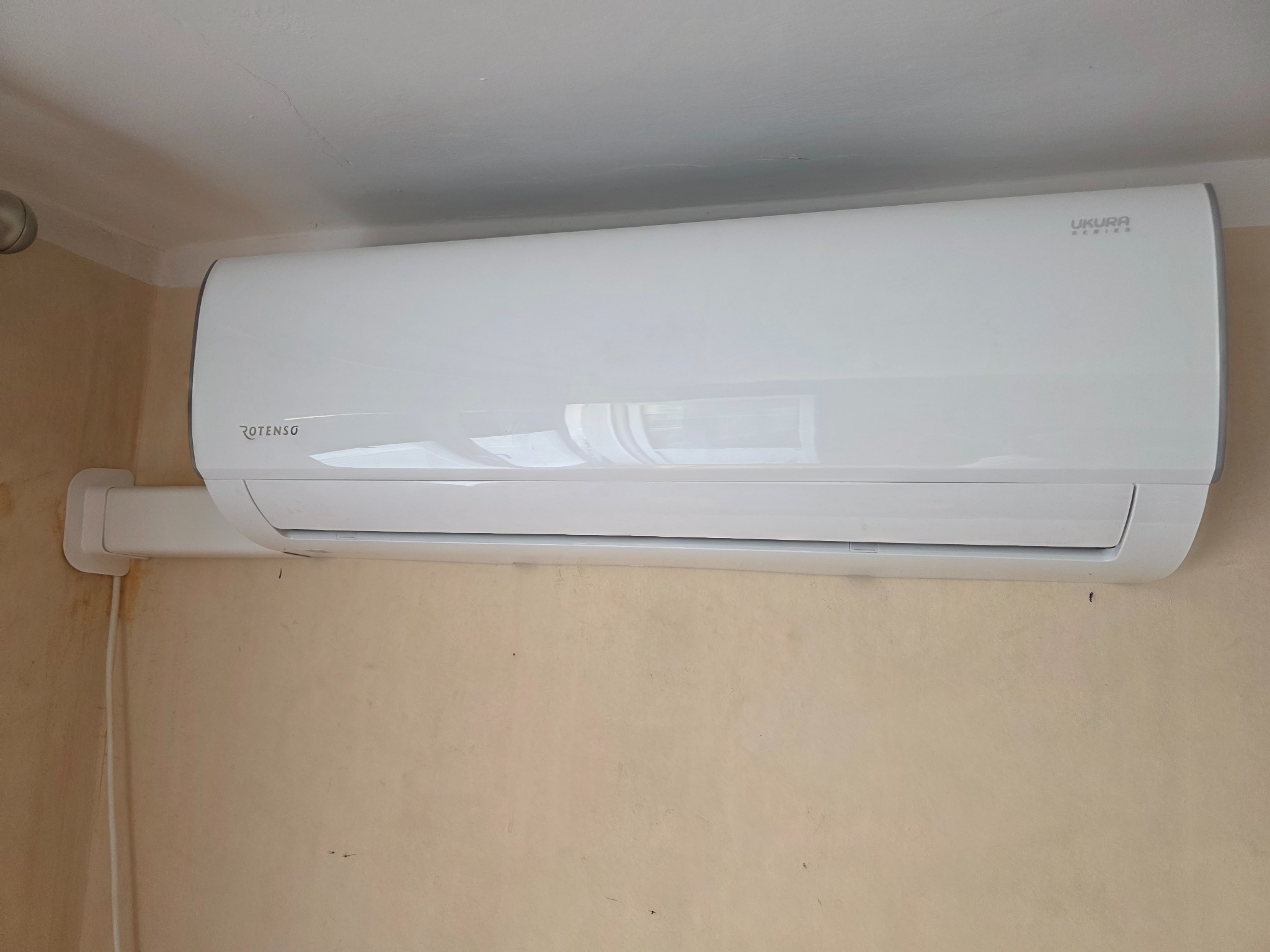 Biała klimatyzacja Rotenso Ukura Series zamontowana na ścianie w pomieszczeniu. Widoczne detale instalacji i połączenia.