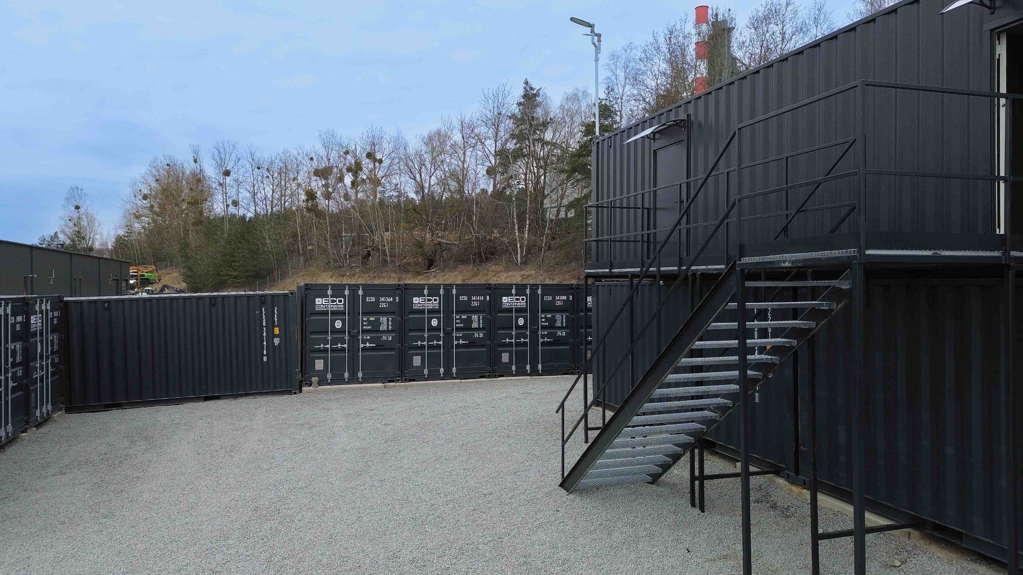 Kontenery magazynowe w Gdańsku. Widok na dwukondygnacyjną konstrukcję z kontenerów z metalowymi schodami i rząd kontenerów w tle.