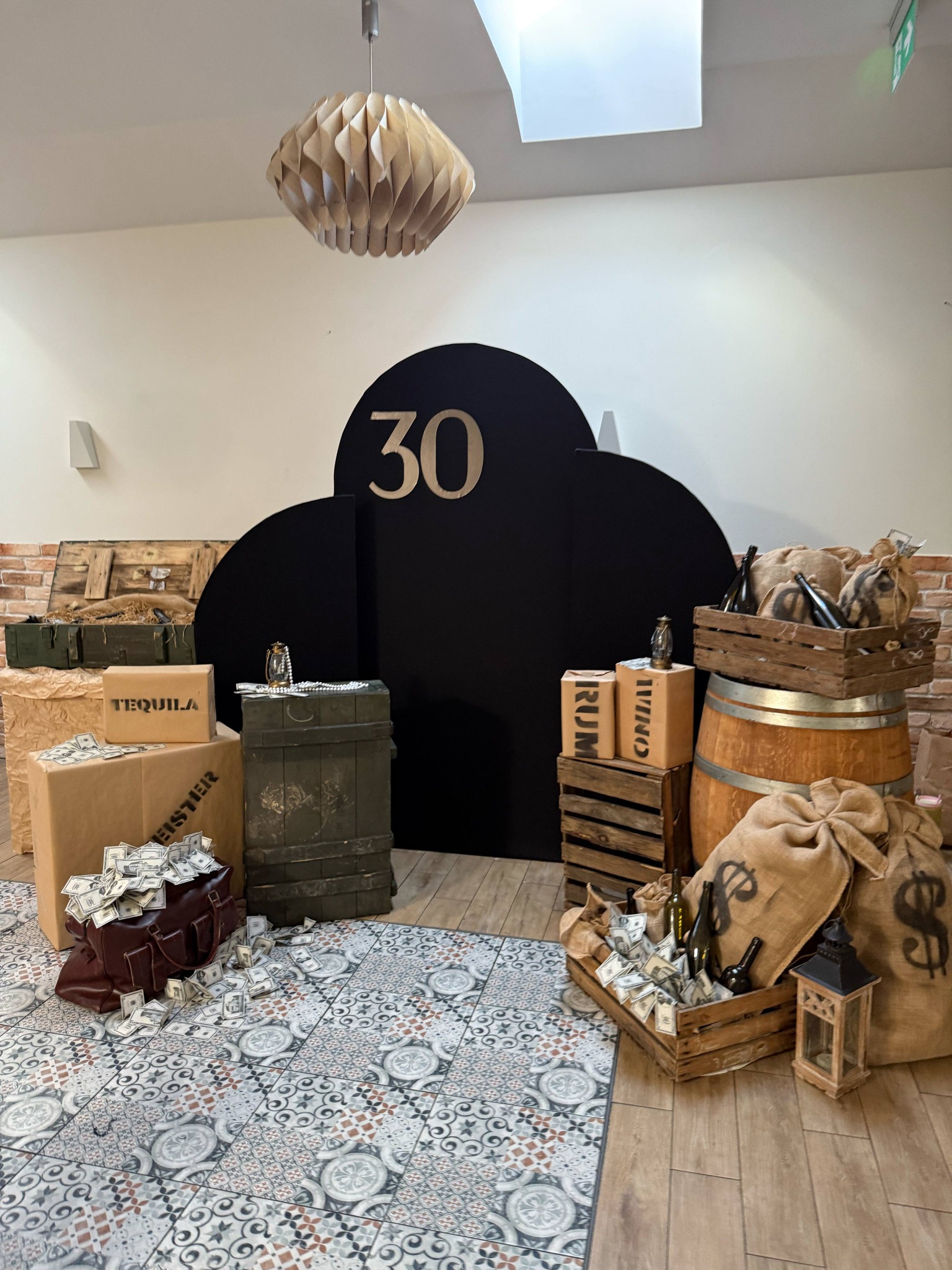 Scenografia urodzinowa w stylu gangsterskim: rekwizyty z beczką, skrzyniami, workami z symbolem dolara i atrapami pieniędzy, czarne tło z liczbą 30.