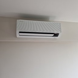 ASPEN Adrian Kosiela - Zamontowany klimatyzator Samsung WindFree na ścianie w Łodzi. Widoczny z bliska, na jasnym tle ściany. Minimalistyczny design urządzenia.