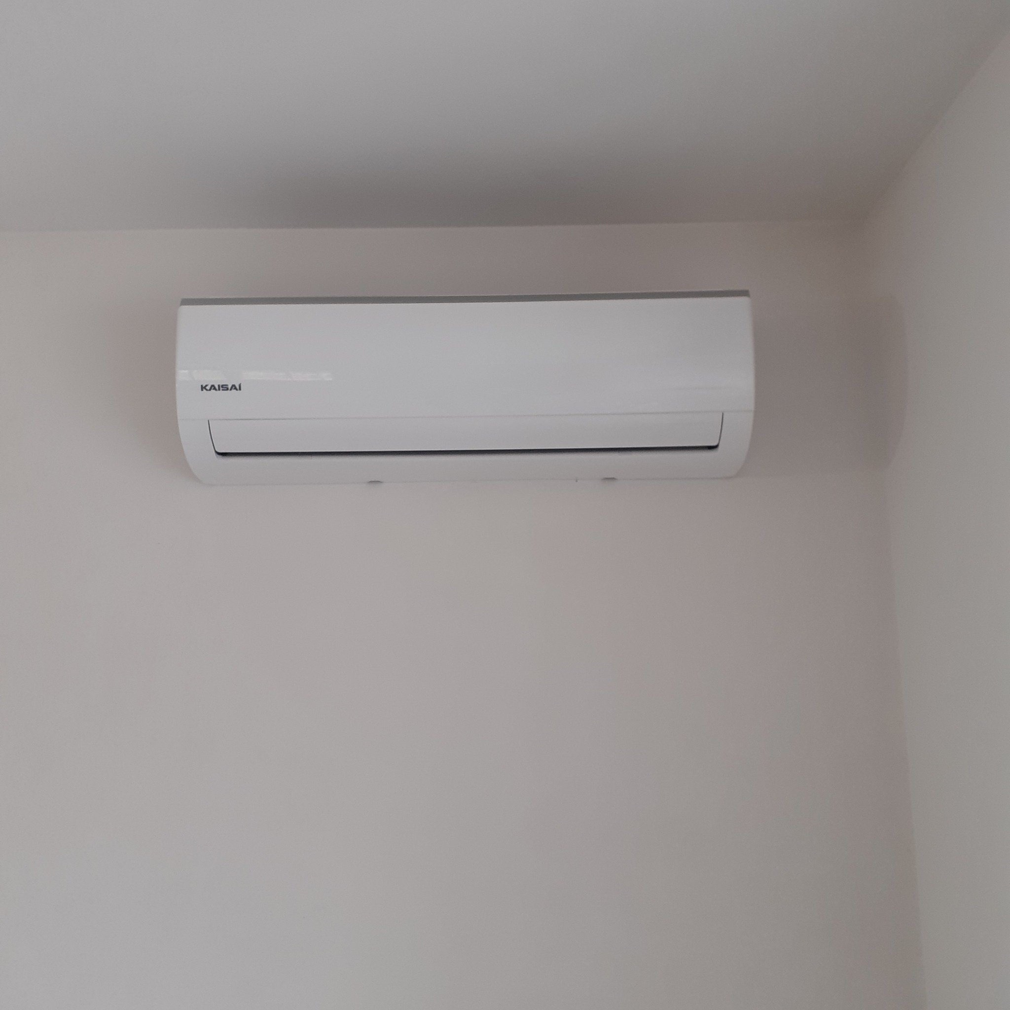 Biała jednostka klimatyzacji Kaisai zamontowana na jasnej ścianie. Widok z dołu, minimalizm i czystość w kadrze.