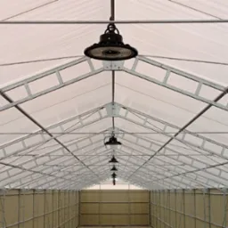 Wnętrze hali z metalową konstrukcją dachu i rzędem okrągłych lamp LED, oświetlających przestrzeń. Widok perspektywiczny w głąb hali.