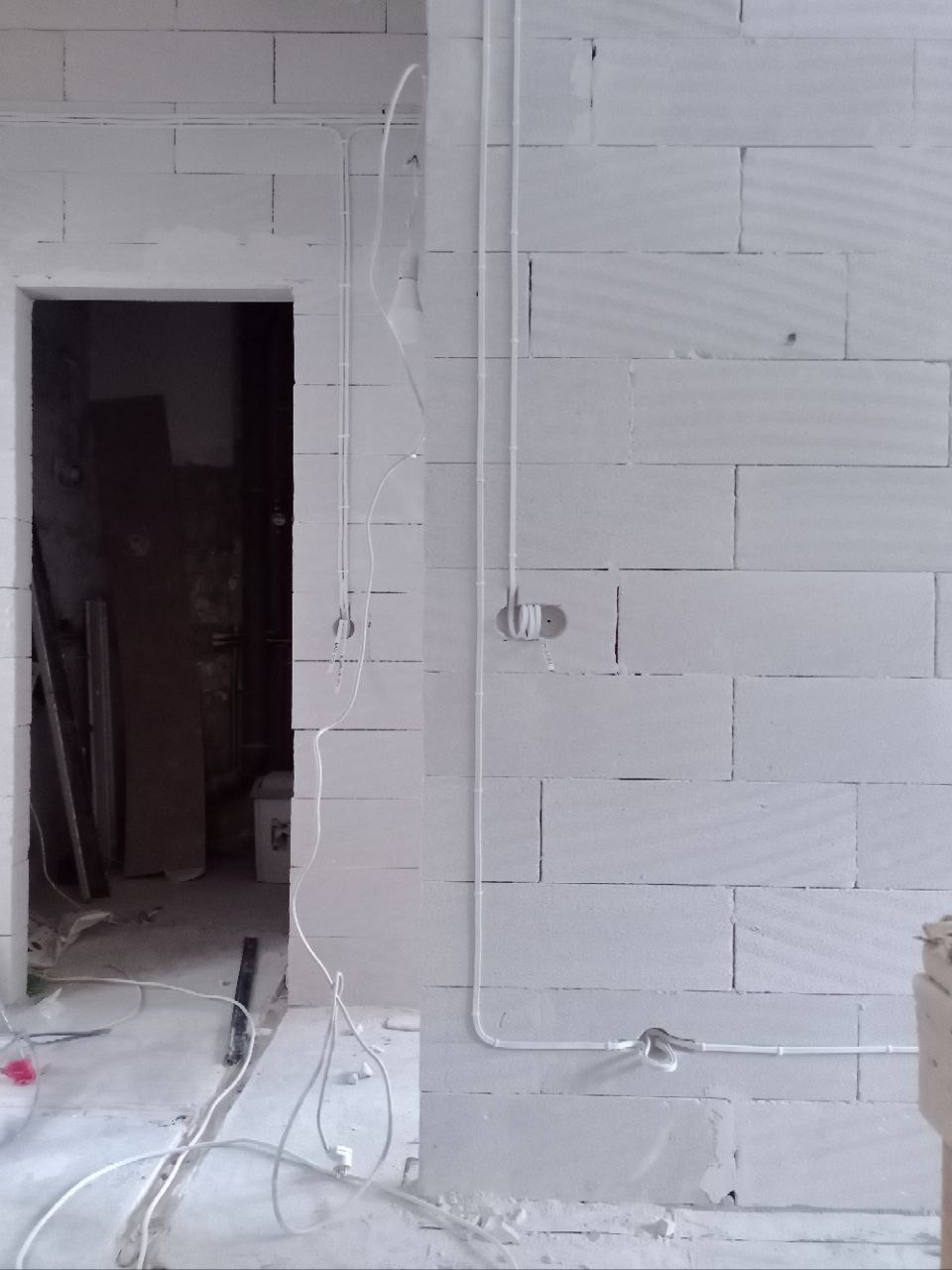 Białe ściany z betonu komórkowego w trakcie instalacji elektrycznej. Widoczne kable i puszki instalacyjne, surowy stan wykończenia, wnętrze w trakcie remontu.