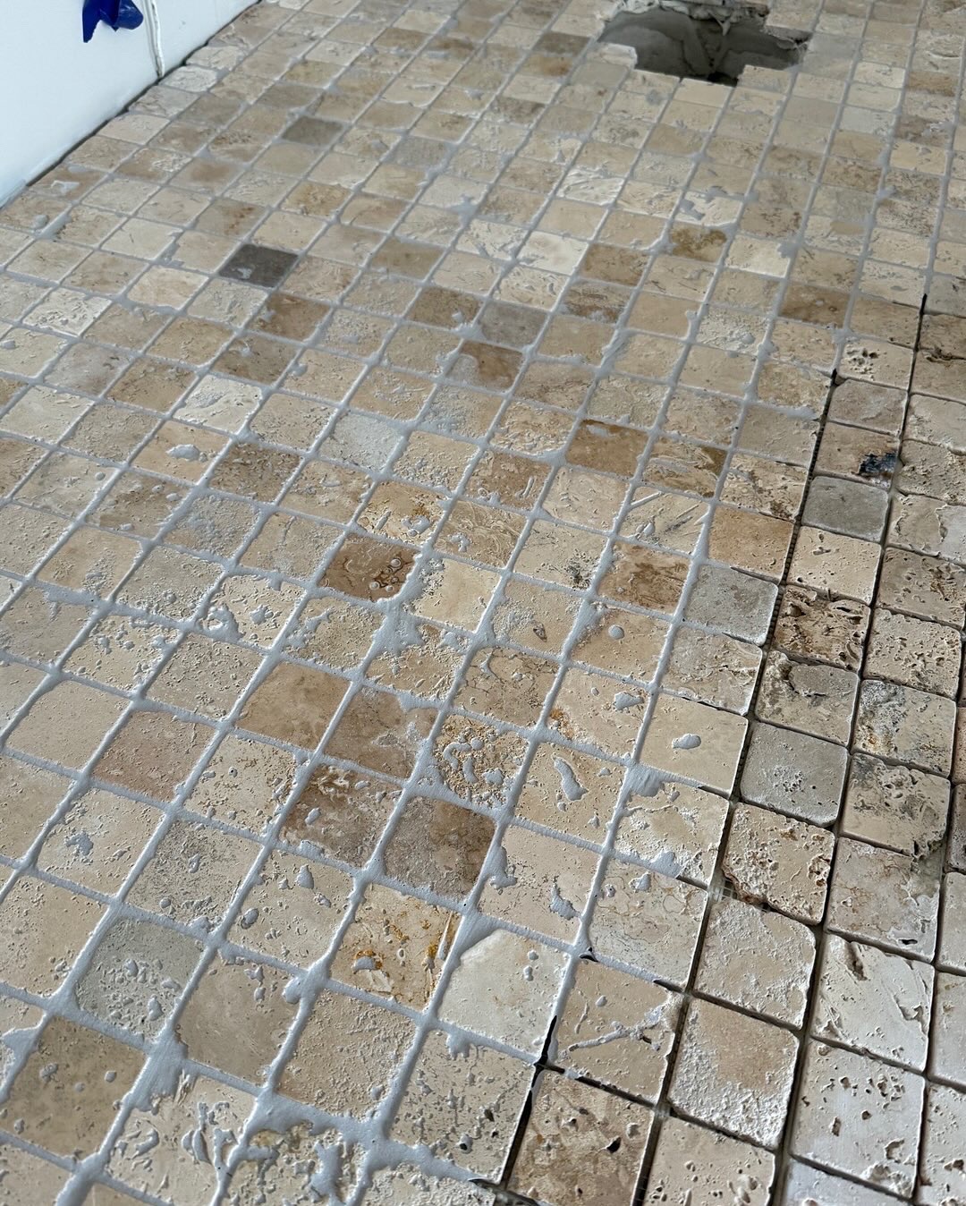 Beżowa mozaika podłogowa z naturalnego kamienia, świeżo ułożona z widocznymi resztkami fugi, z fragmentem niedokończonej powierzchni w rogu.