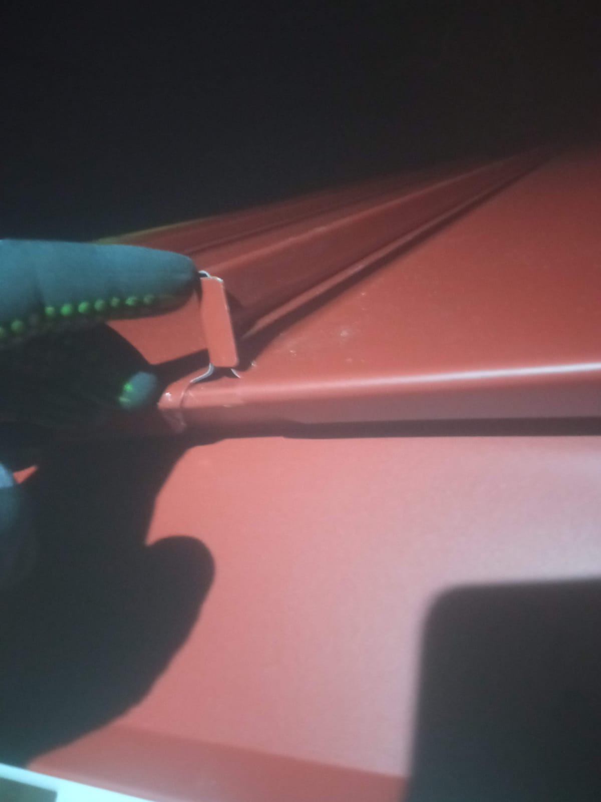 Montaż blachy trapezowej w kolorze ceglastym, widoczna rękawica robocza podczas mocowania elementu.