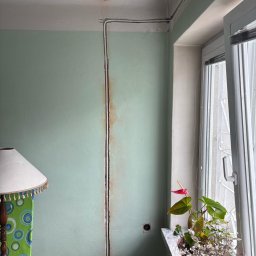 Energofuse Technology - Bruzdowanie ściany pod instalację elektryczną w pomieszczeniu z zieloną ścianą i oknem. Widoczne kable pod sufitem. Etap prac przed tynkowaniem.