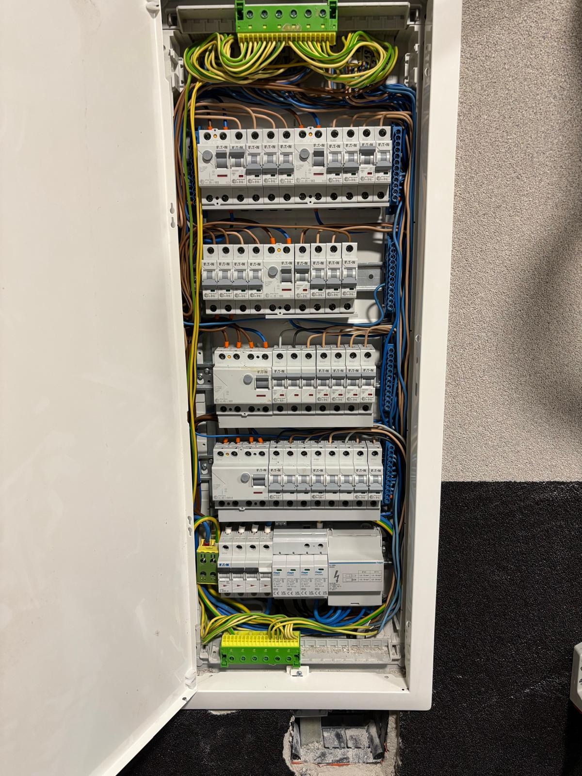 Otwarta skrzynka elektryczna z bezpiecznikami, widoczne kable i listwy zaciskowe. Instalacja elektryczna w budynku, wykonana schludnie i profesjonalnie.