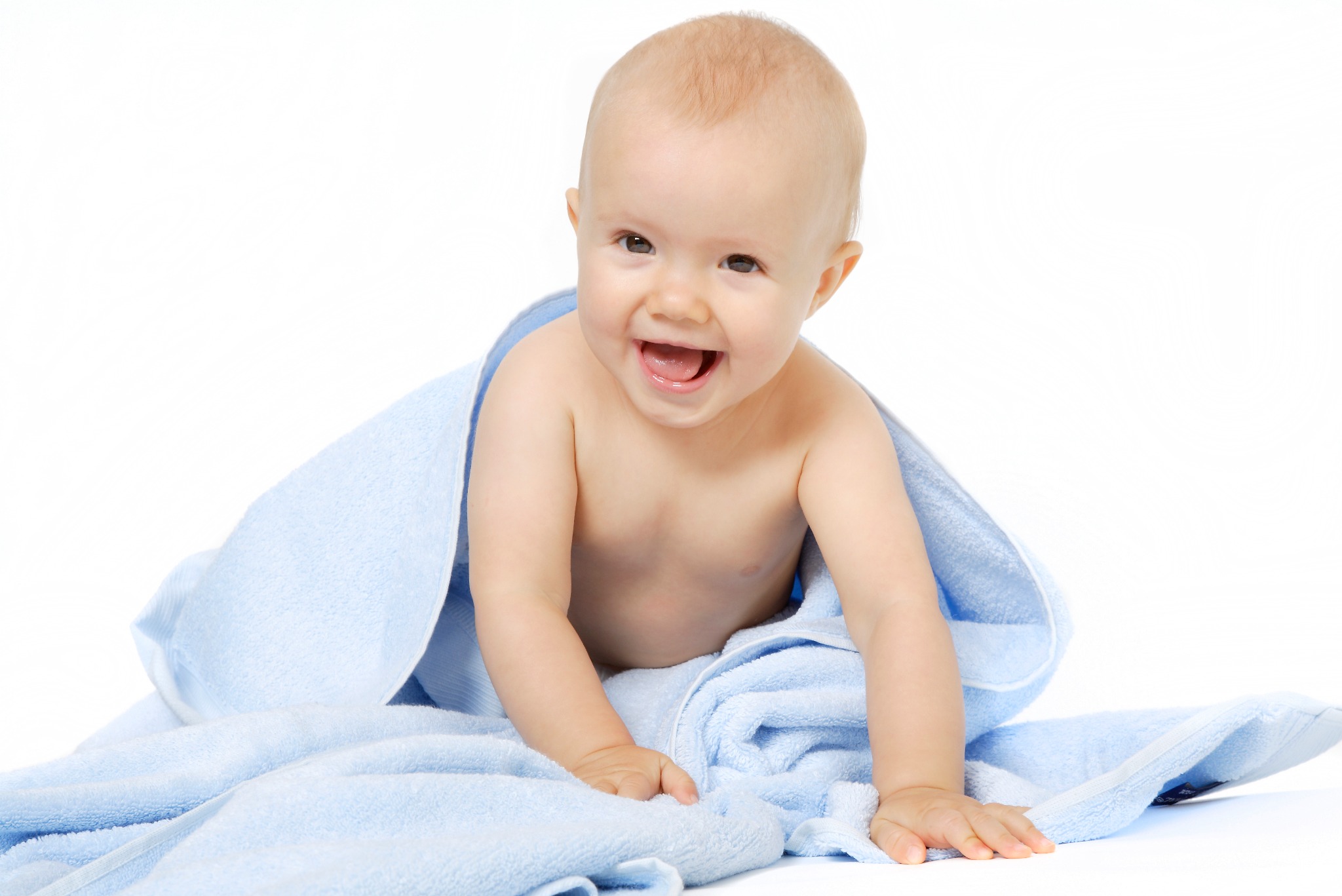 Uśmiechnięty niemowlak w błękitnym ręczniku, na białym tle. Dziecko raczkuje w kierunku obiektywu, z otwartymi ustami i radosnym wyrazem twarzy. Jasne, równomierne oświetlenie.