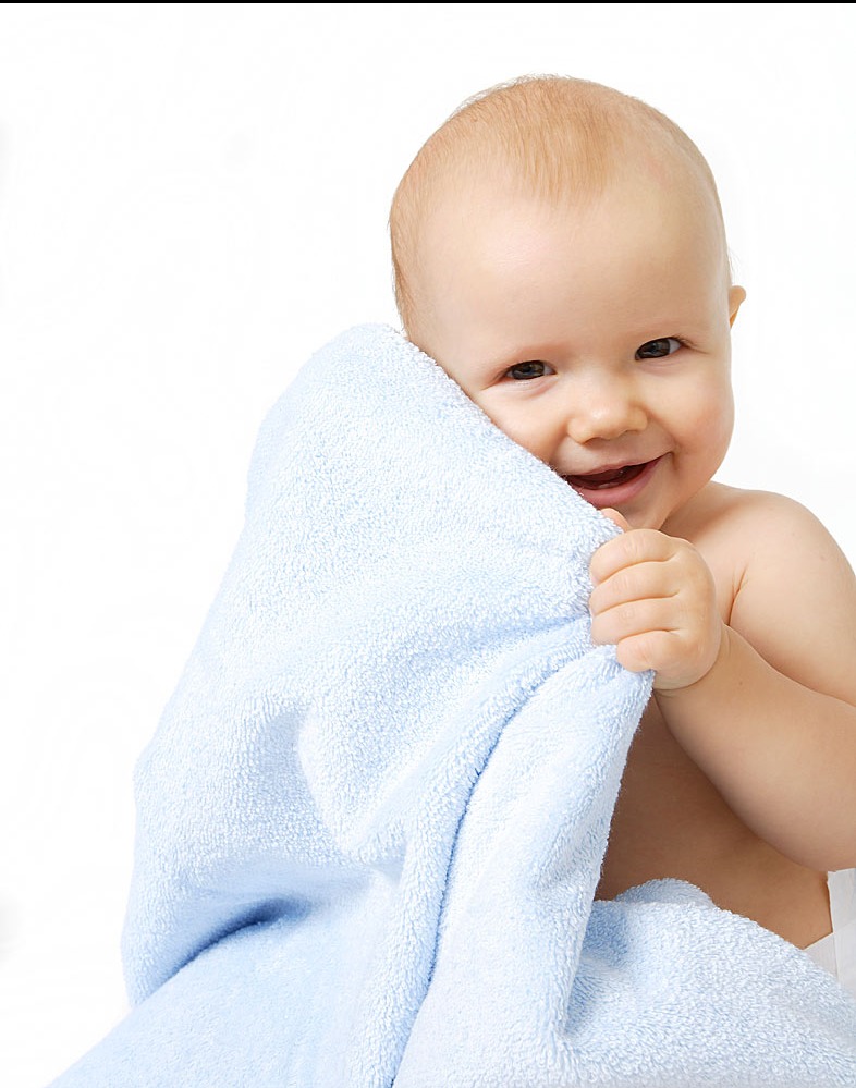Uśmiechnięte niemowlę, owinięte w błękitny, puszysty ręcznik na białym tle, trzymające brzeg ręcznika w dłoni. Dziecko patrzy w obiektyw.