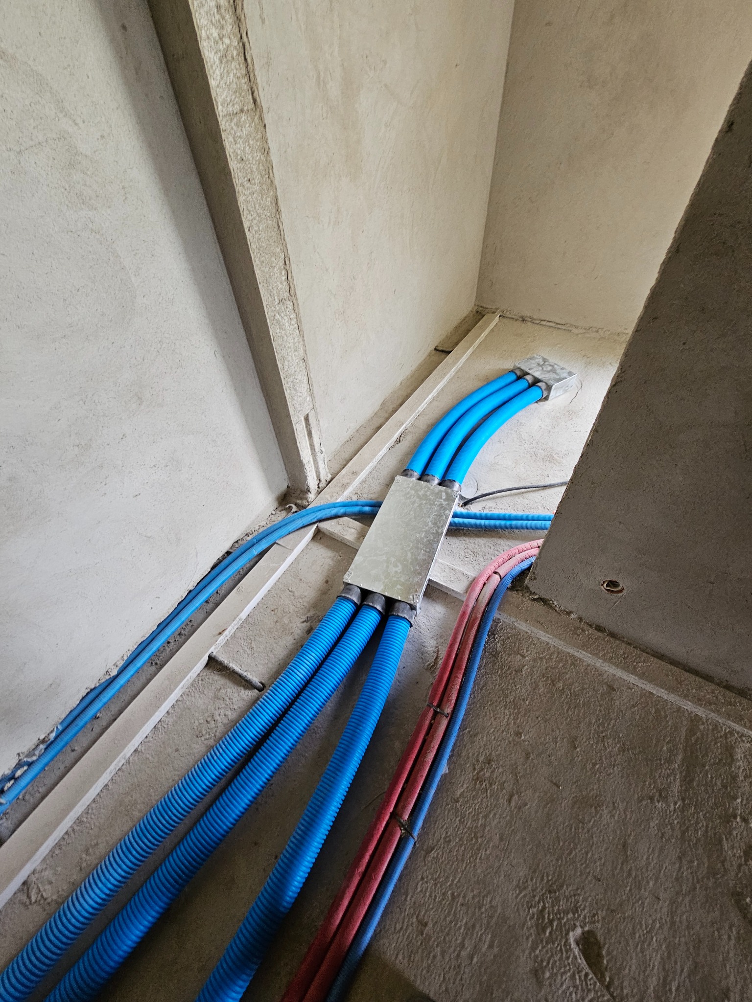 Niebieskie i czerwone rury wentylacyjne ułożone w surowym pomieszczeniu przed dalszymi pracami wykończeniowymi, widoczne złącza i fragmenty ścian.