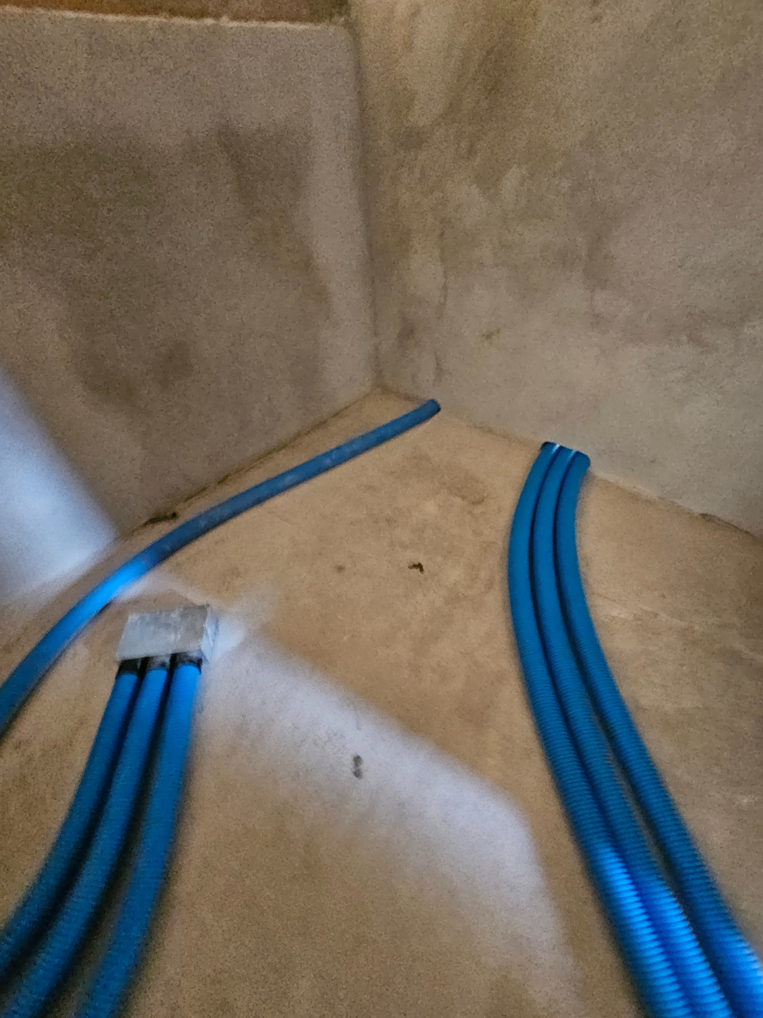 Niebieskie, karbowane rury wentylacyjne w rogu surowego pomieszczenia, prawdopodobnie w trakcie montażu systemu wentylacji mechanicznej.