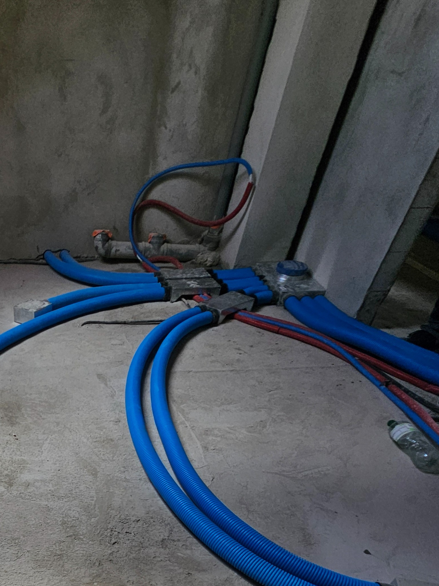 Rozprowadzenie instalacji wentylacyjnej z niebieskich rur karbowanych, widoczne elementy montażowe i rury w kolorze czerwonym. Surowy stan wykończenia.