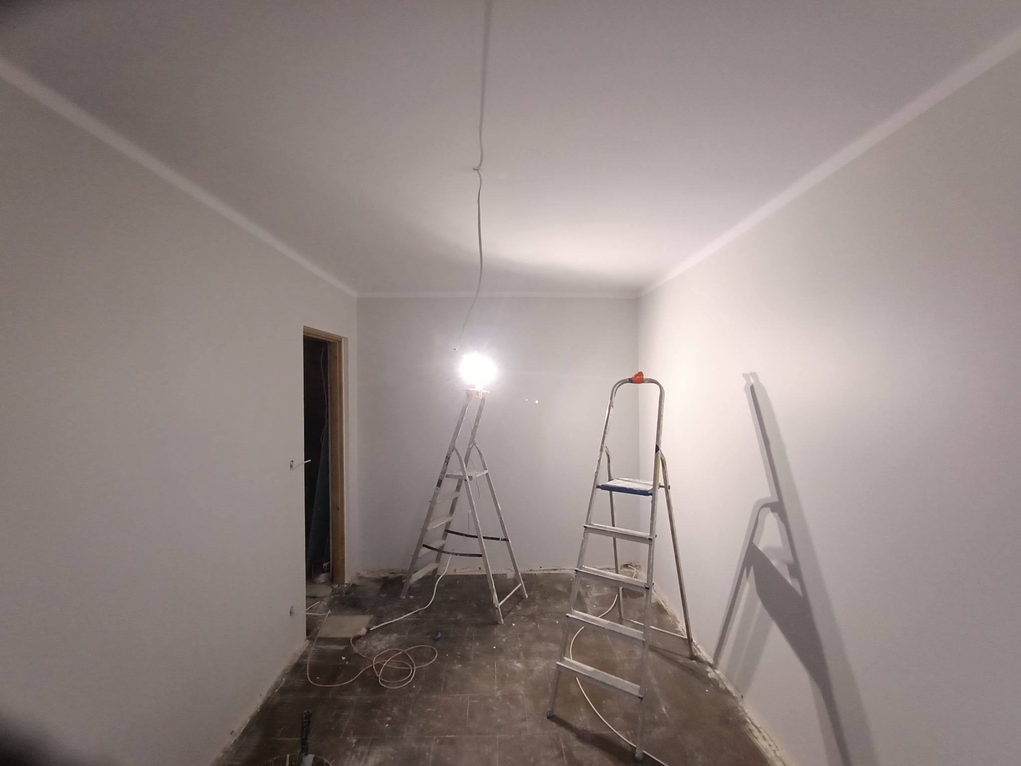 Wnętrze pokoju po malowaniu ścian na biało, widoczne dwie drabiny malarskie, podłoga zabezpieczona folią malarską, listwy przypodłogowe pomalowane.