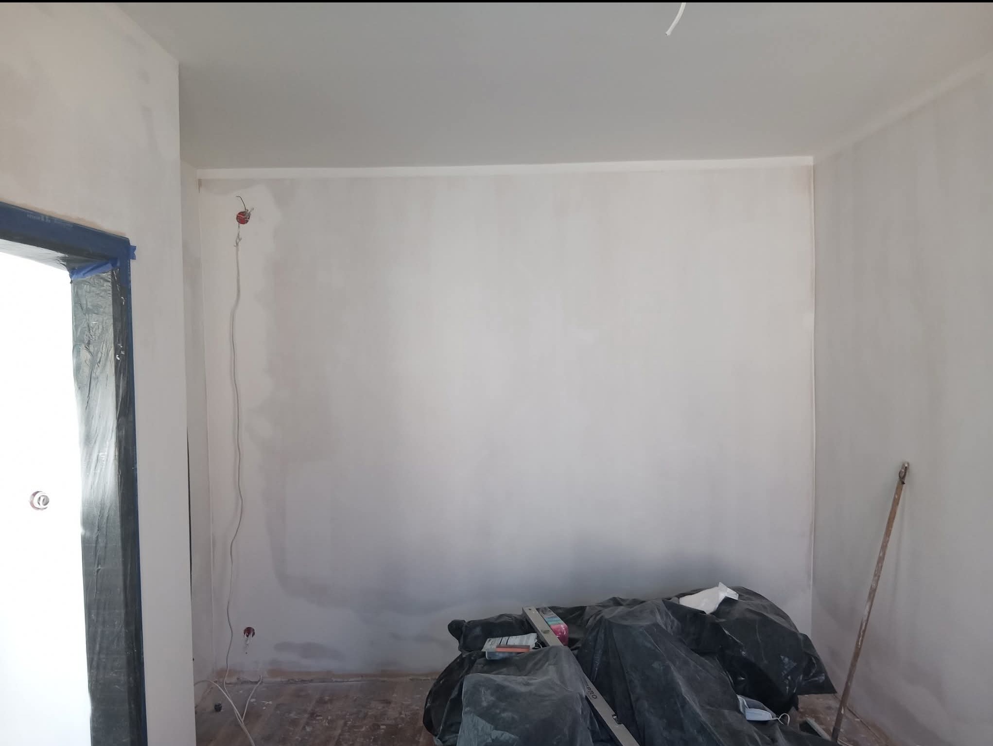 Pokój w trakcie szpachlowania ścian, widoczne narzędzia i worki z odpadami. Otwór drzwiowy zabezpieczony folią malarską. Ściany przygotowane do dalszych prac.