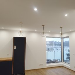 Artur Jagielski - Nowoczesna kuchnia z czarnymi szafkami, drewnianym blatem i trzema szklanymi lampami wiszącymi. Widok na zewnątrz przez duże okno.